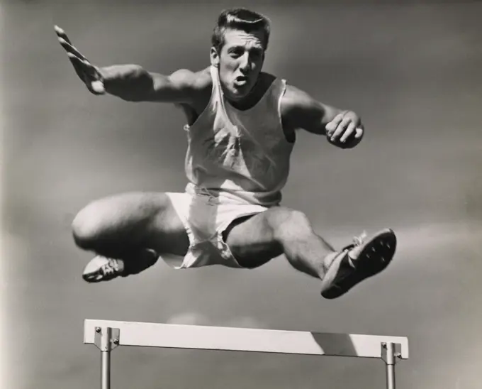 Low angle view of a male athlete jumping over a hurdle