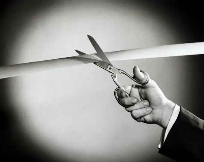 Person's hand cutting a ribbon with a pair of scissors