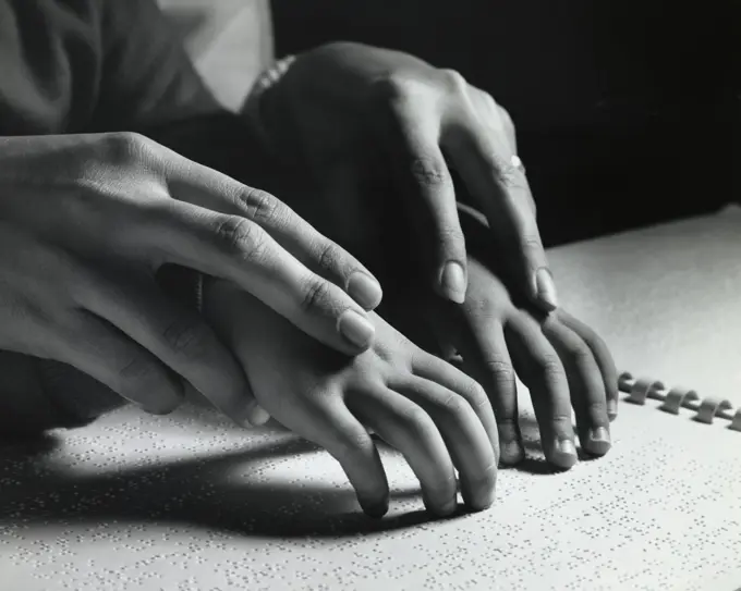 Close-up of an adult helping a blind child read Braille script