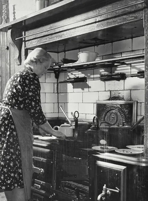 Vintage photograph. Side profile of a mature woman preparing meal in typical Northern Ireland farm kitchen