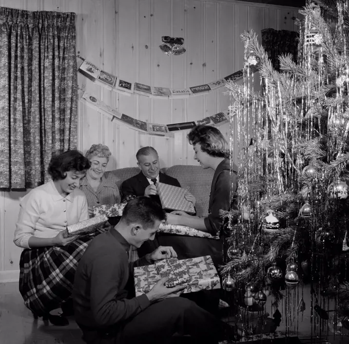 Family opening gifts by Christmas tree in living room