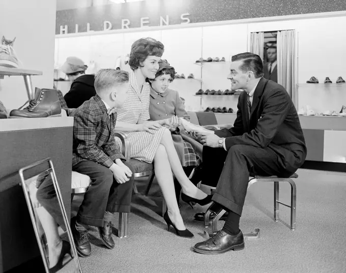 Shop assistant showing women's shoe to mother with son and daughter