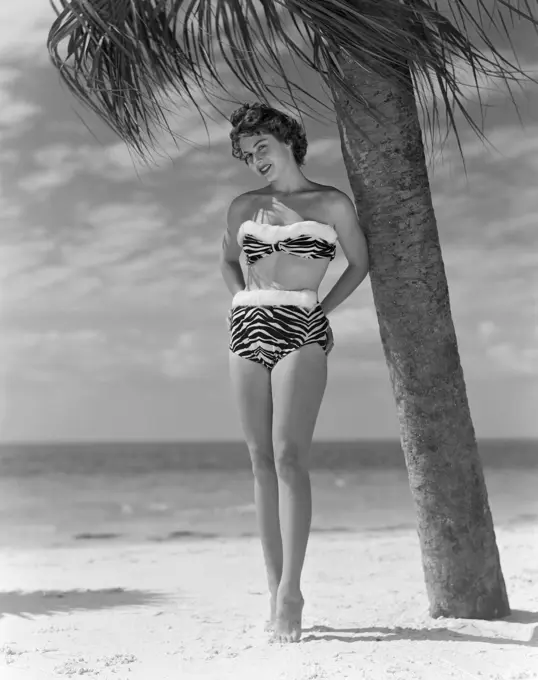 Pin-up girl standing under palm tree, wearing bikini