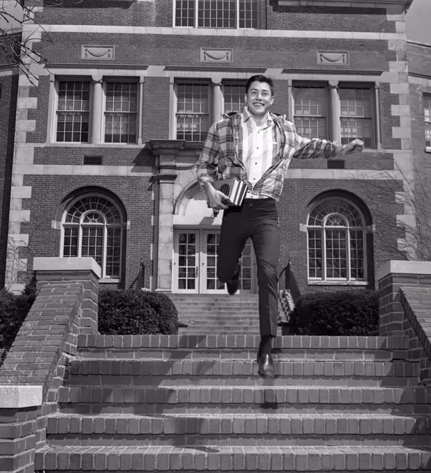 Male student jumping down steps outside university