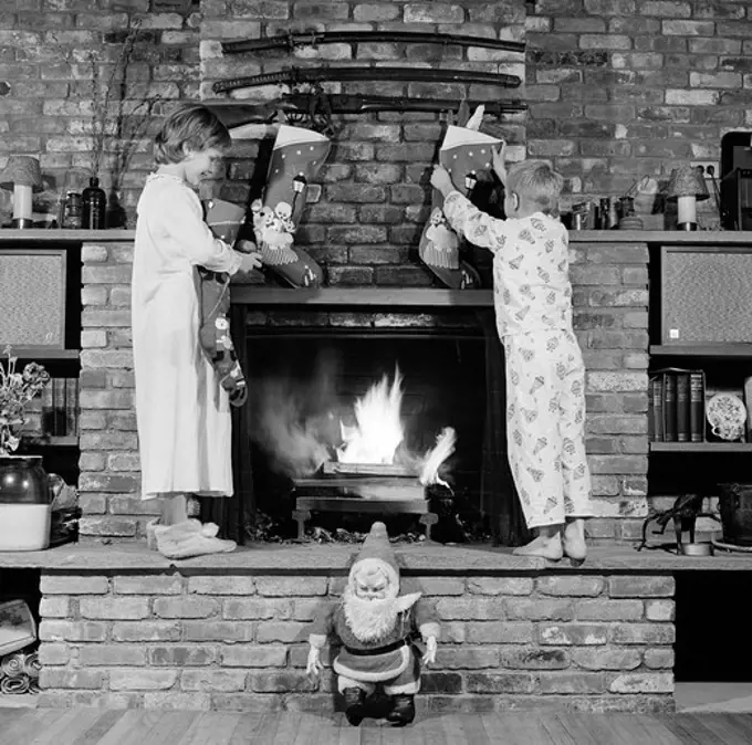 Girl and boy decorating fireplace with christmas stockings