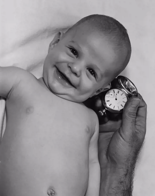 Smiling baby and hand of adult man holding watch