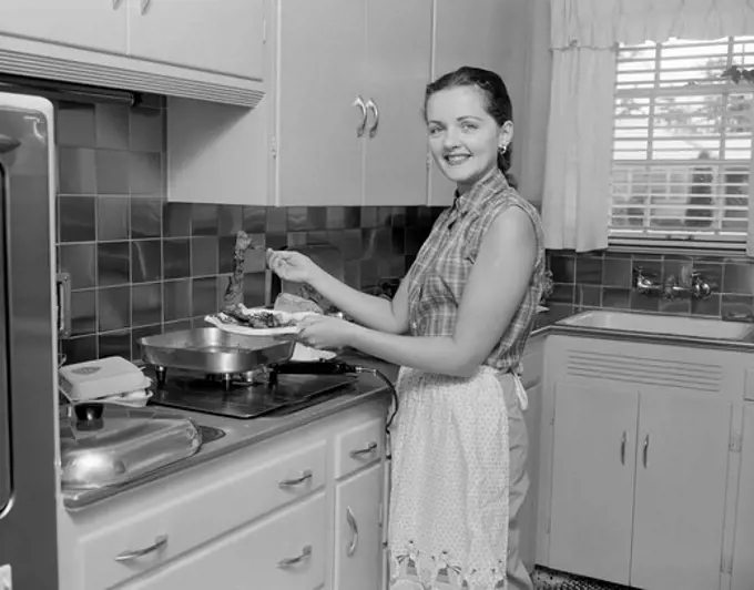 Woman holding plate with food in the kitchen and looking at camera