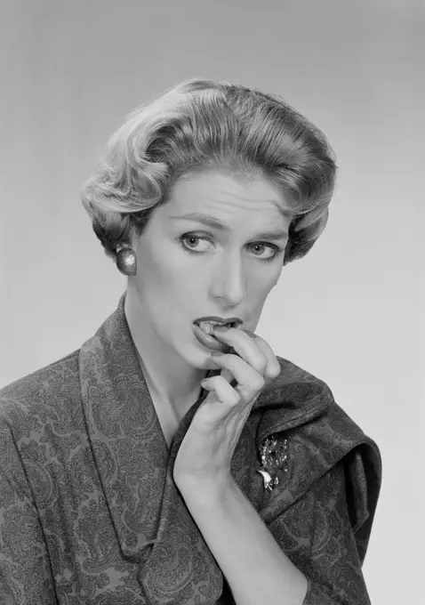 Mid adult woman biting her nails and looking away, studio shot