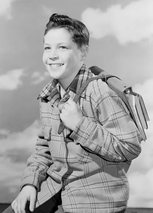 School boy carrying books against cloudy sky