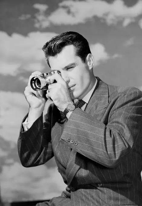 Young man using camera against cloudy sky