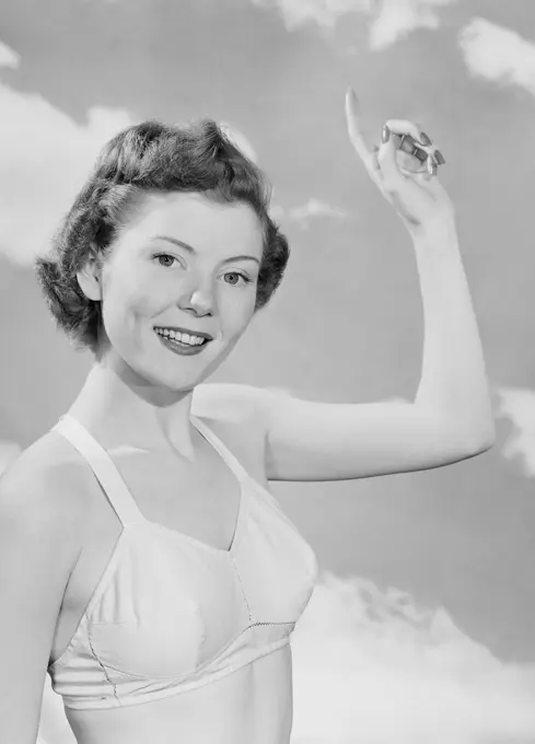 Portrait of woman pointing up against cloudy sky