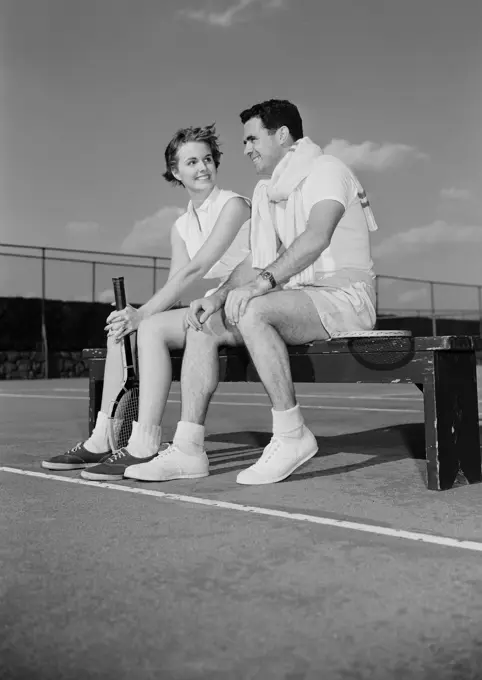 Young couple sitting by tennis court