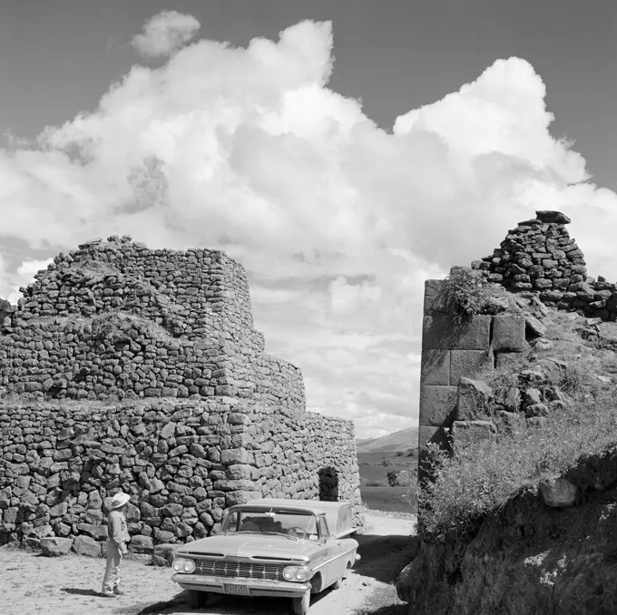 Peru, man standing next to his car among old ruins