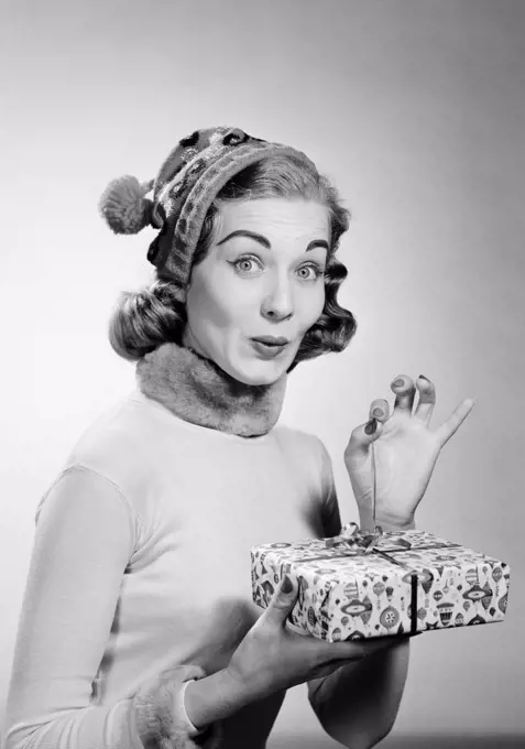 Young woman wearing knit hat opening christmas gift