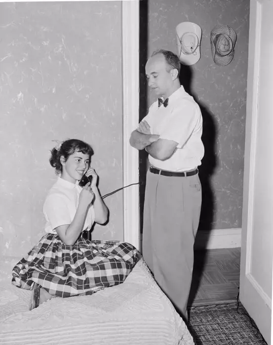 Father watching teenage daughter using telephone in home