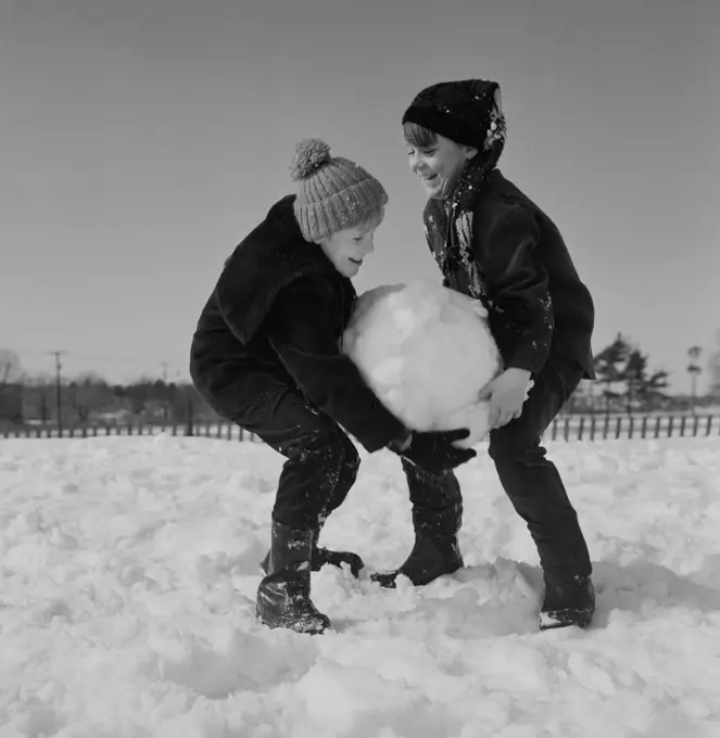 Two kids carrying large snowball