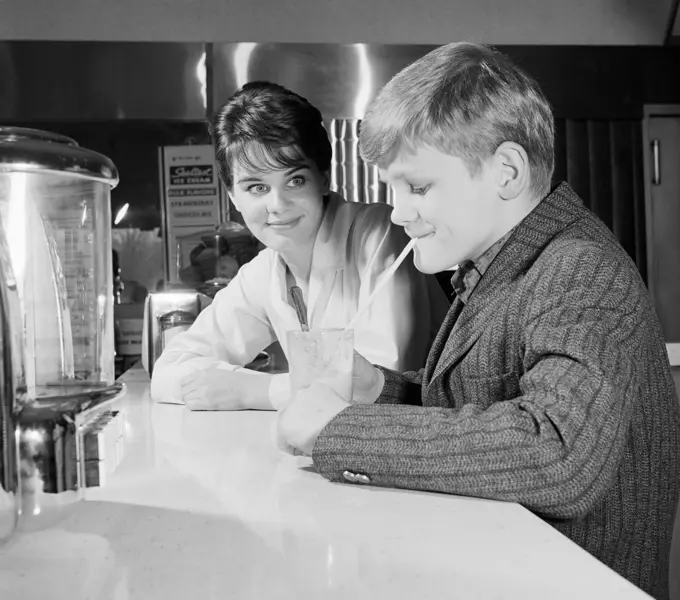 Woman looking at boy drinking milk shake