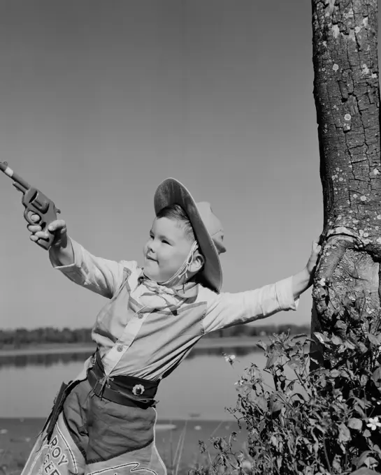 Boy dressed as cowboy playing with toy gun