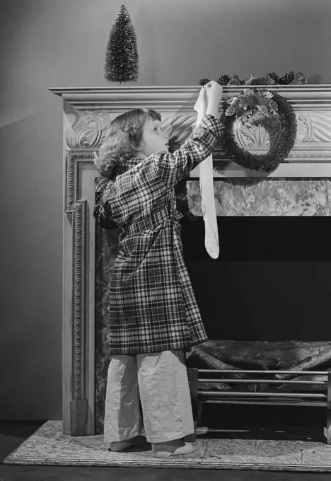 Girl hanging Christmas stocking on mantelpiece