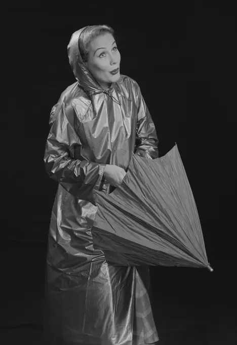 Young woman wearing raincoat opening umbrella