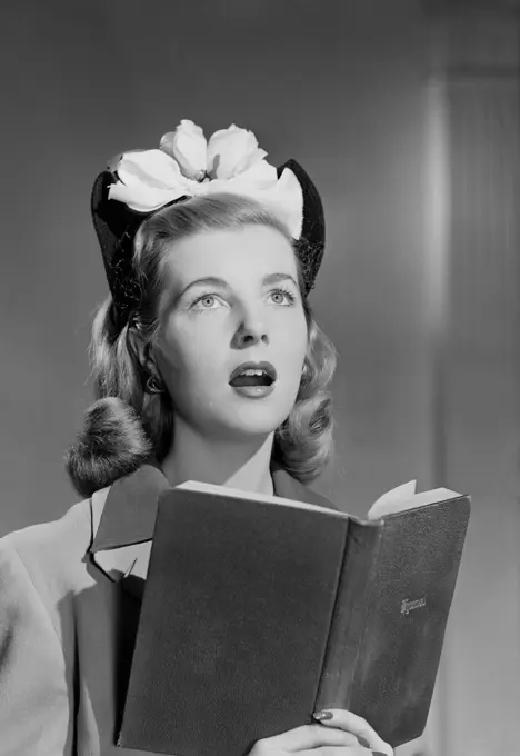 Female choir singer holding book, singing indoors