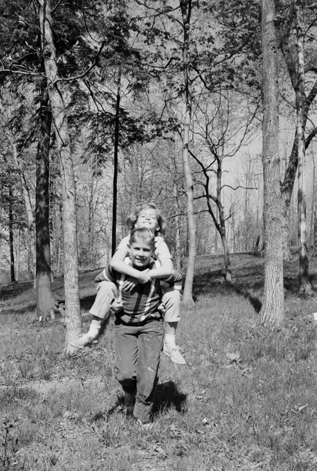 Girl piggyback riding on boy in forest