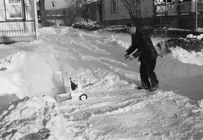 Mature man clearing snow from approach to suburban home