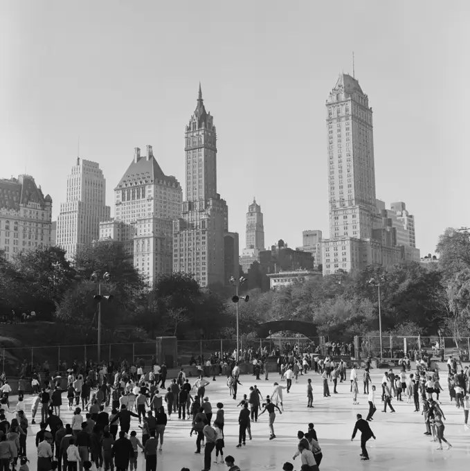 USA, New York City, Central Park, People ice-skating in front of skyline