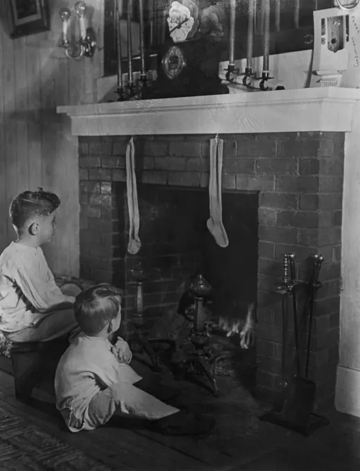 Two boys (4-5) sitting in front of fireplace looking at christmas stockings