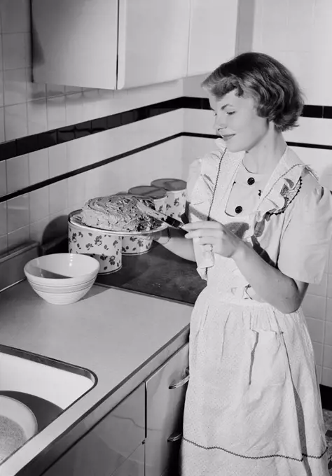 Young woman icing cake in kitchen