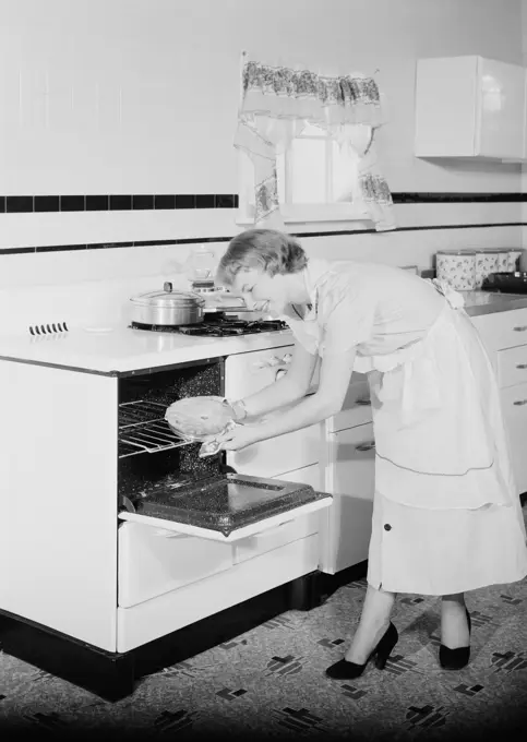 Young woman taking pie from oven in kitchen