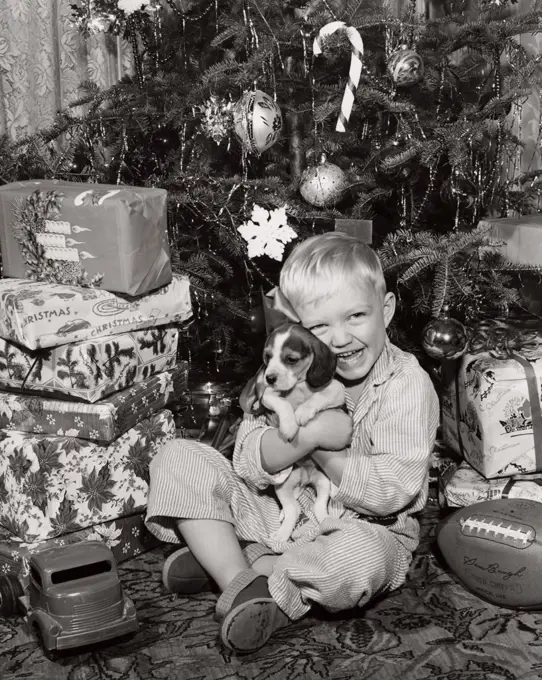 Portrait of a boy sitting near Christmas presents and hugging his puppy