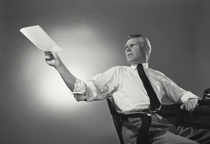 Vintage Photograph. Man in button shirt and tie leaning back and passing a document. Frame 1