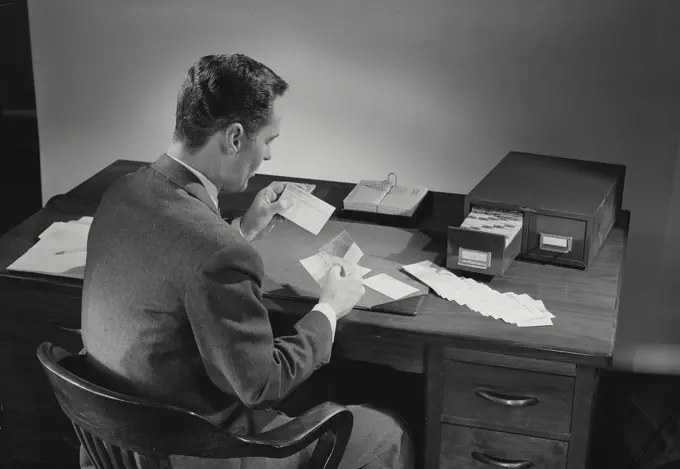 Vintage Photograph. Man in suit sitting at desk covered in papers. Frame 2