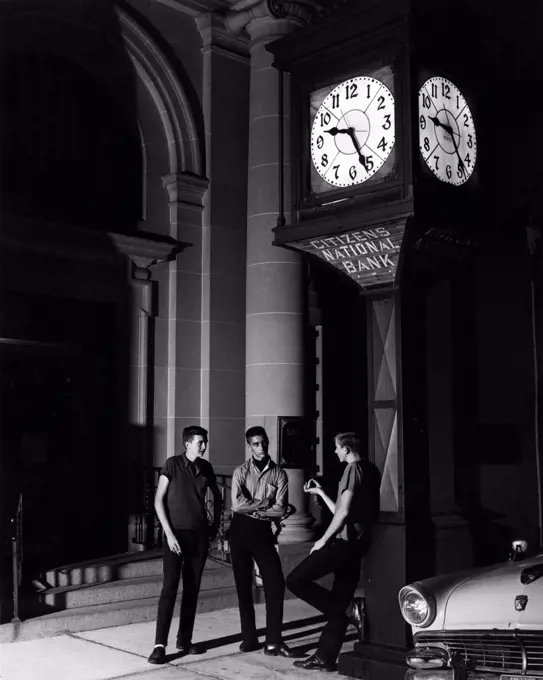 Three men having conversation outside bank at night