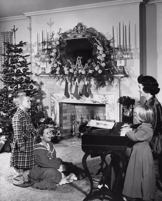 Mid adult woman playing a piano and her three children looking at her