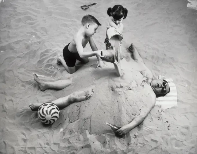 High angle view of a brother and his sister burying their father on the beach