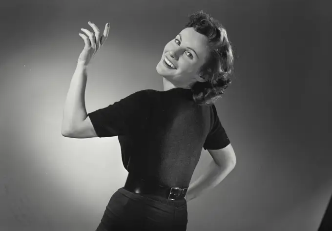 Vintage Photograph. Woman in black dress smiling over shoulder with hand up