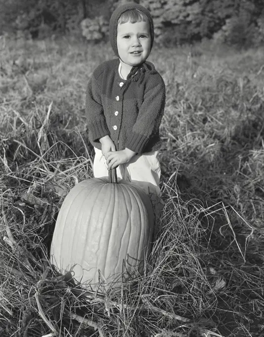 Model Release. Jodene Scaylea. Vintage Photograph. A little girl standing behind a large pumpkin.