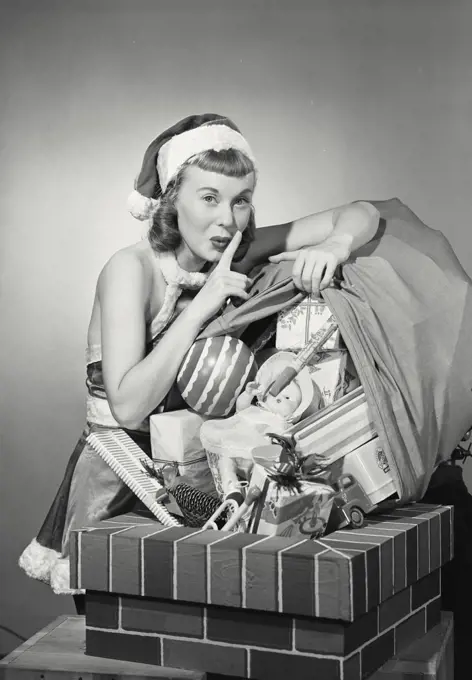 Vintage photograph. Portrait of a young woman dressed as santa quietly dumping toys down chimney