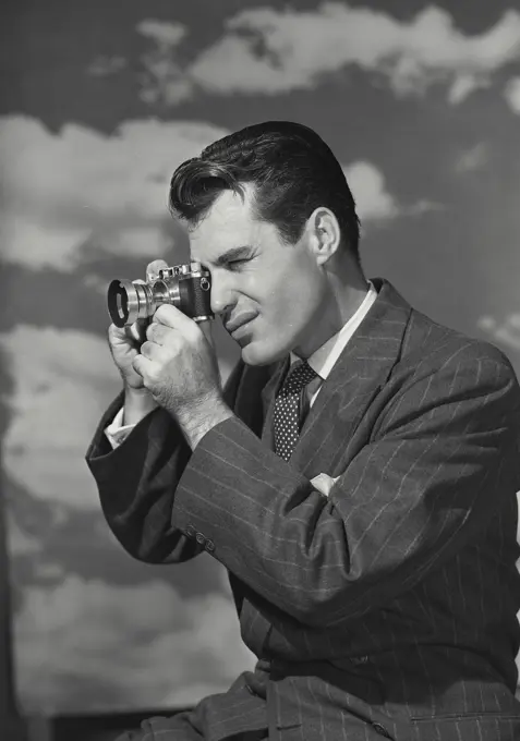 Vintage Photograph. Man looking through camera in front of cloud sky background