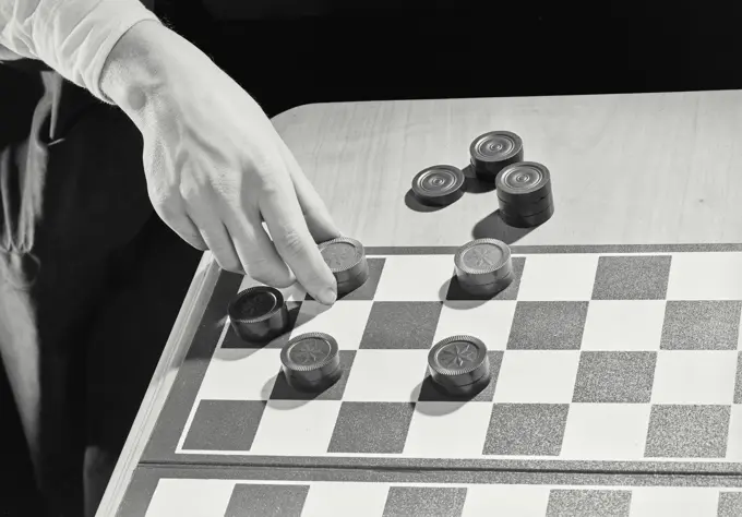 Vintage photograph. Hand grabbing stacked checkers pieces from board