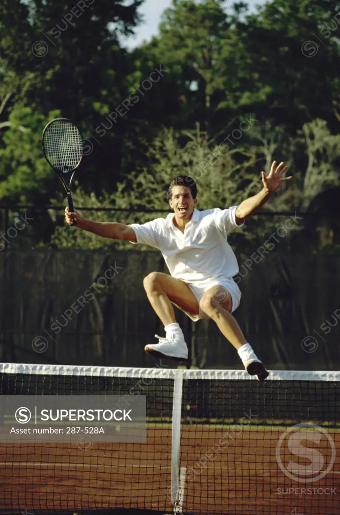 Mid adult man jumping over a tennis net