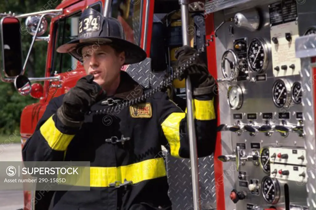 Firefighter standing near a fire engine and talking on a walkie-talkie