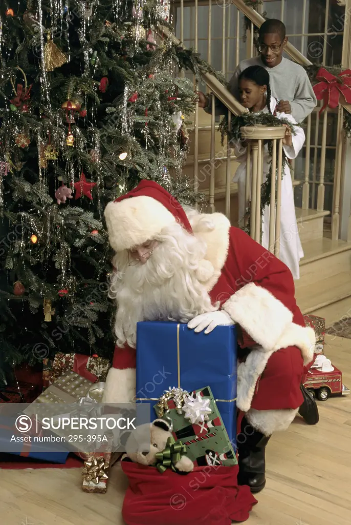 Santa Claus putting Christmas gifts beside a Christmas tree