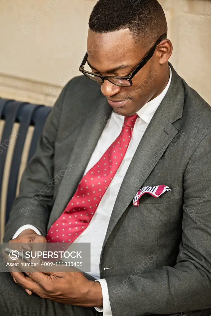 Black businessman using cell phone on bench