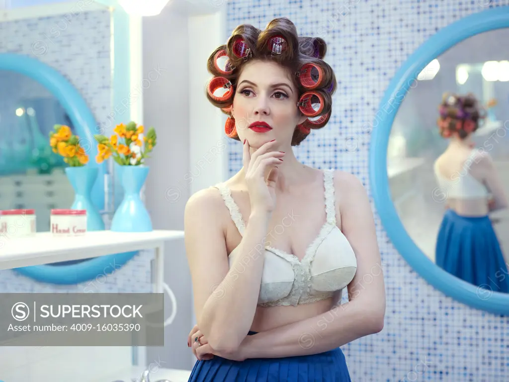 Portrait of vintage styled woman in a mid-century bathroom, with hair curlers in her hair.