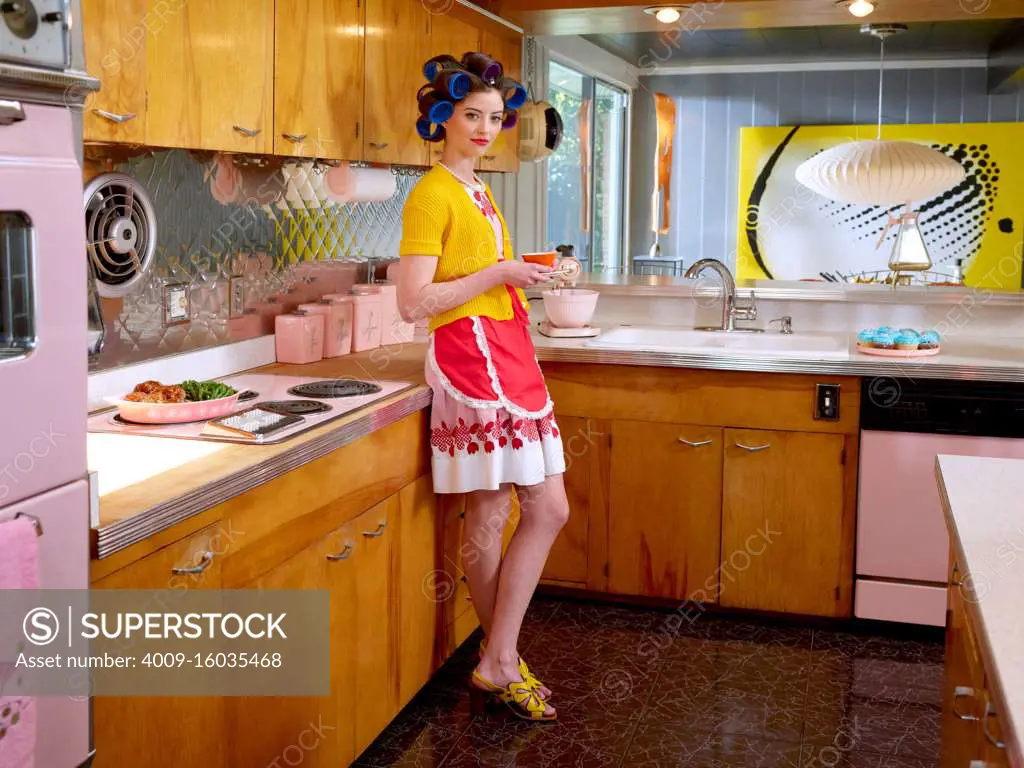 Vintage-styled woman holding a coffee looking into camera in a mid century house. 