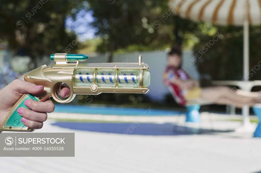 Vintage toy ray gun in womans hand pointing in the direction of out of focus man in the background.