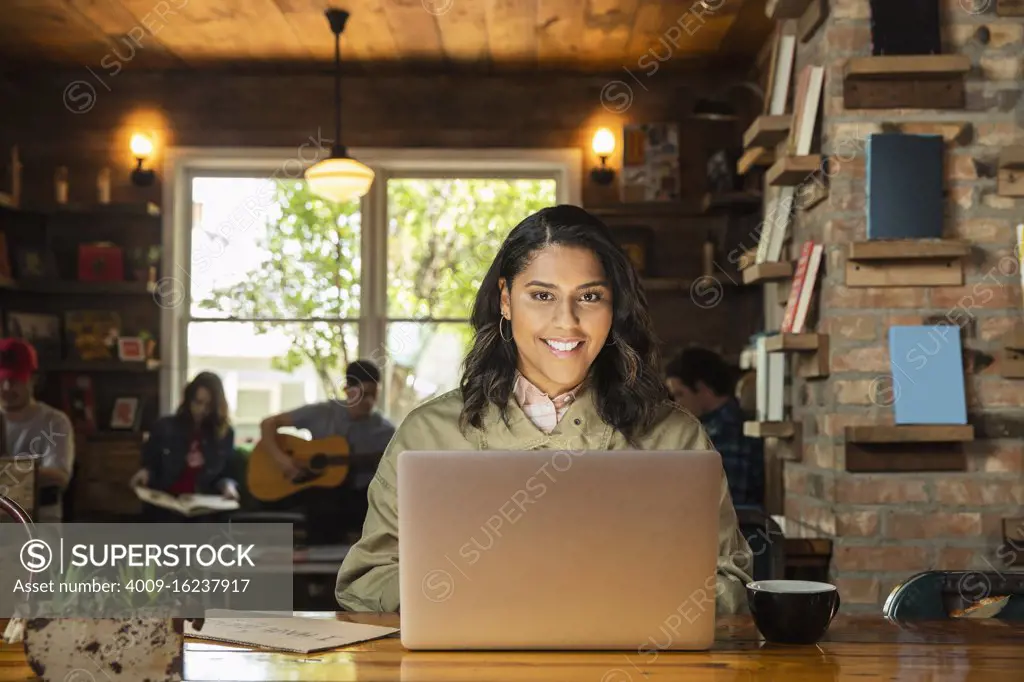 Portrait of young woman sitting at table in coffee shop bookstore using laptop computer 